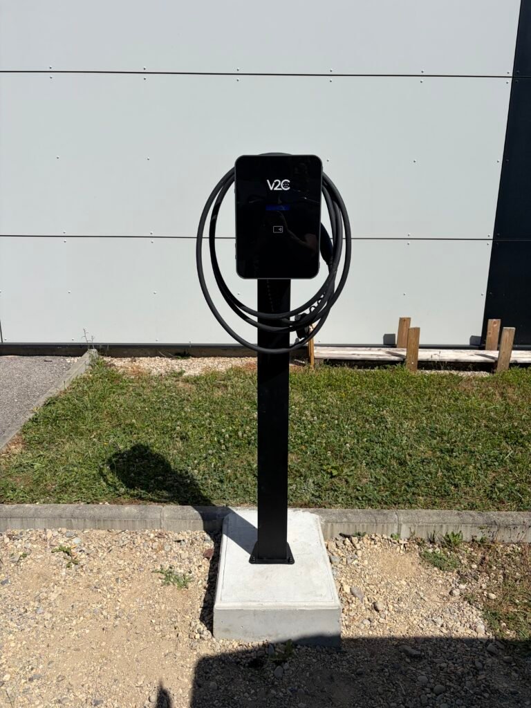 Borne de recharge V2C installée sur un pied en béton dans un jardin